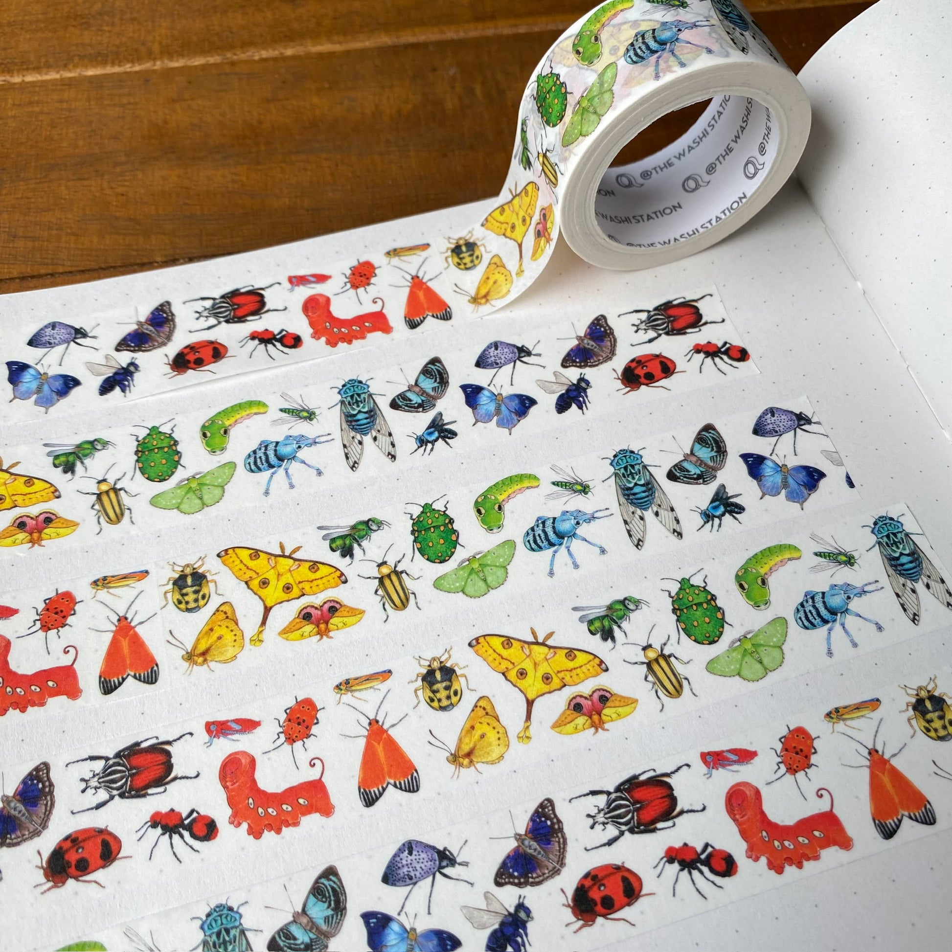 Washi tape with insects arranged in rainbow order swatched in a dot grid notebook.