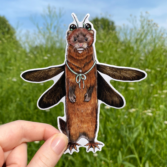 A hand holding a weatherproof vinyl sticker of an American mink dressed up as a damselfly.