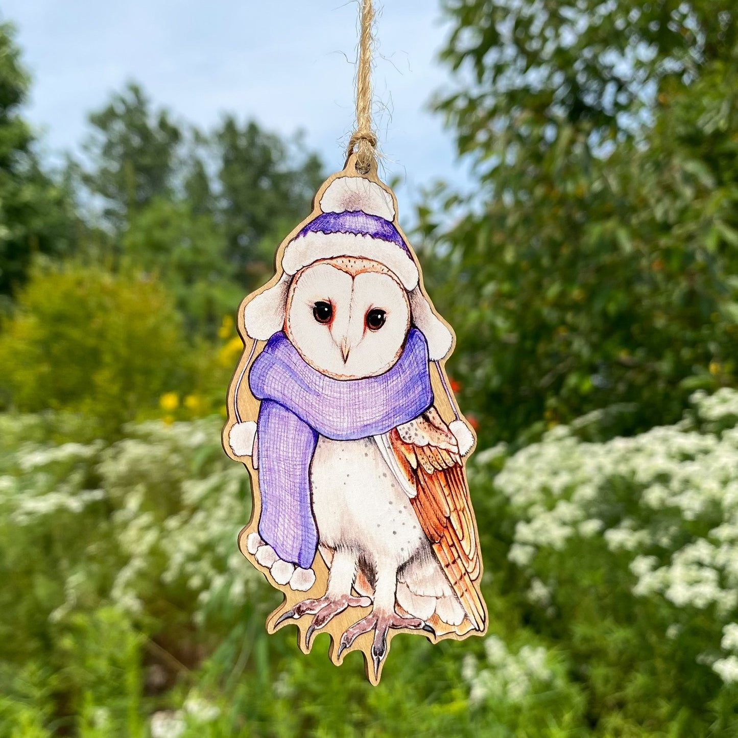 A wooden ornament strung with twine of a barn owl in a purple scarf and hat.