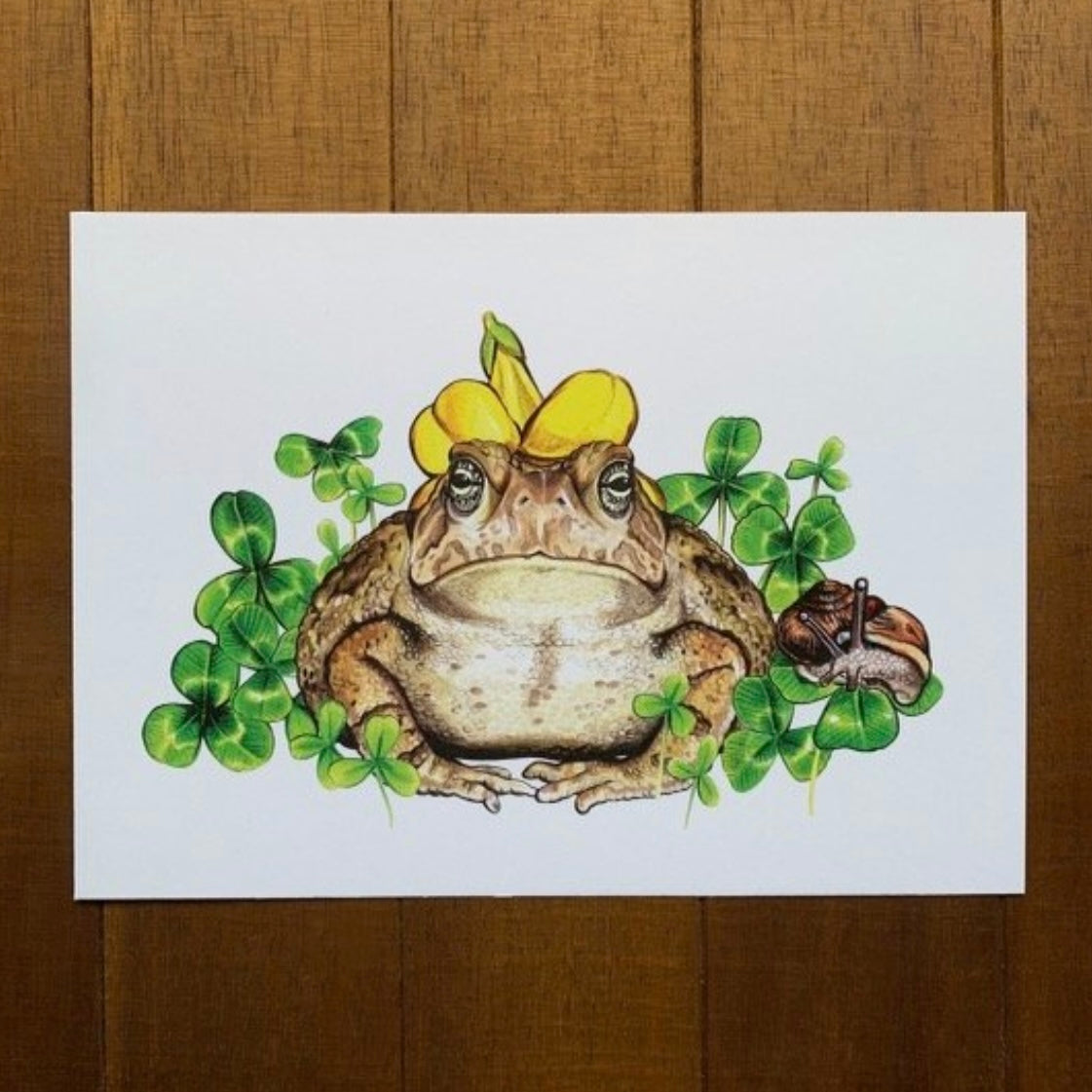 A 5" by 7" print of a Fowler's toad in a flower hat surrounded by clover and a snail.