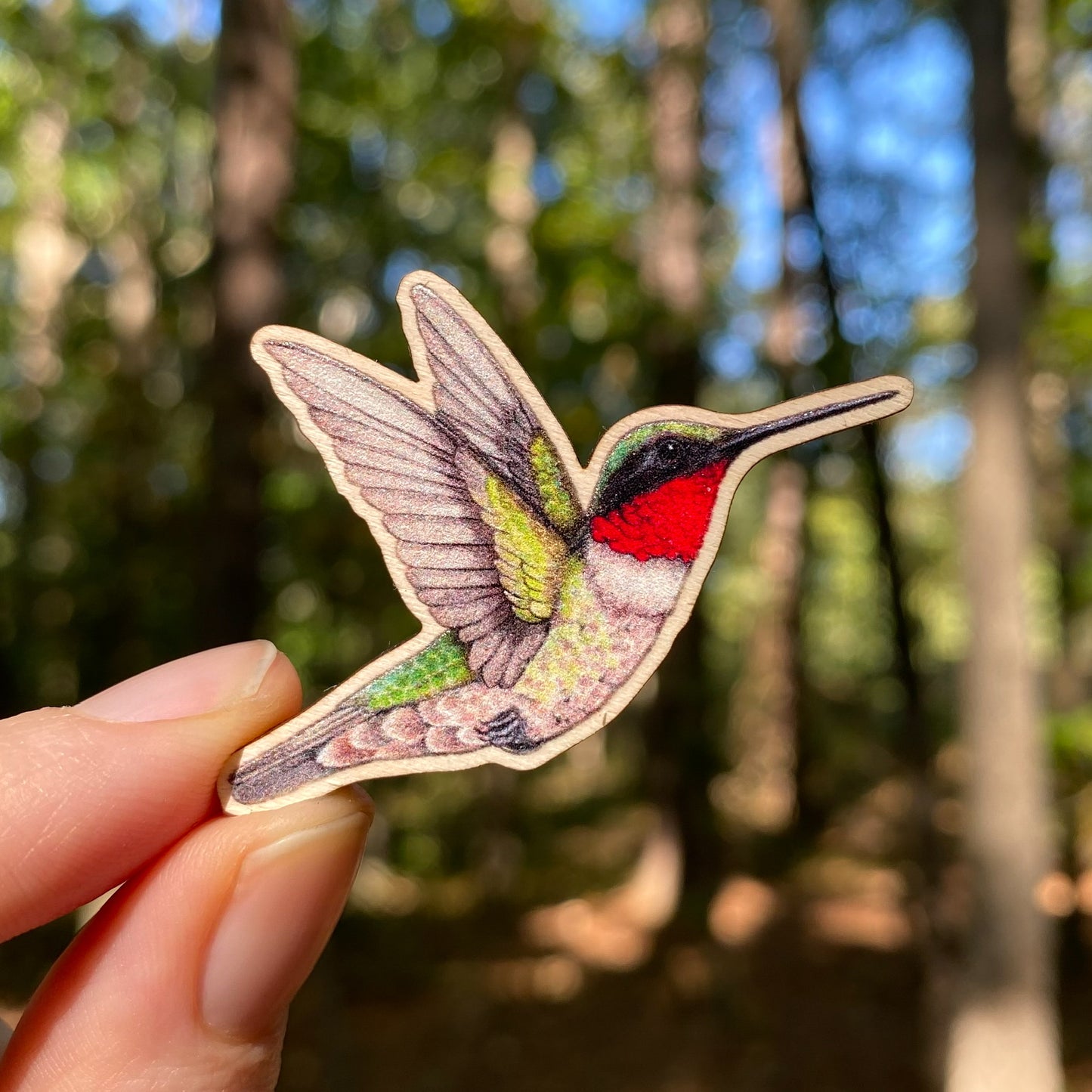 A wooden pin of a male ruby-throated hummingbird on a white background.