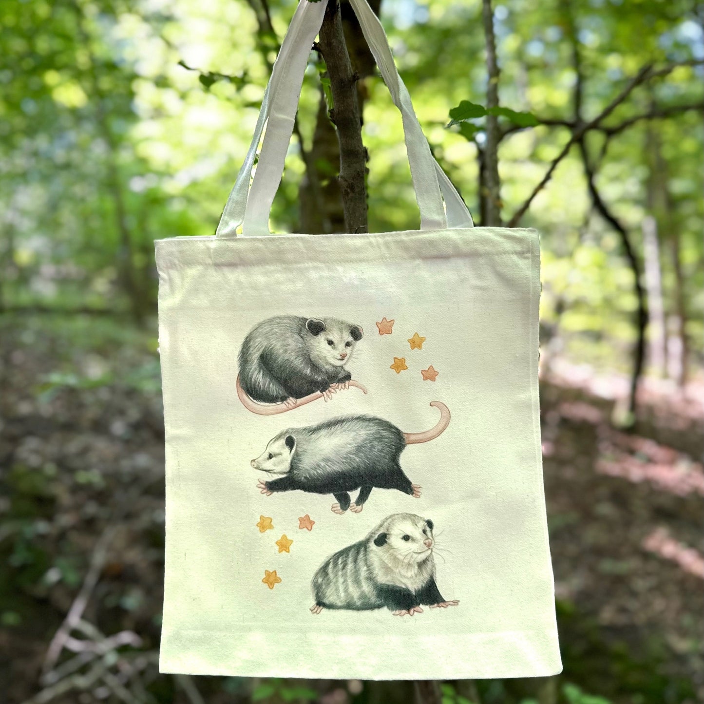 A tote bag featuring an illustration of a trio of opossums and stars