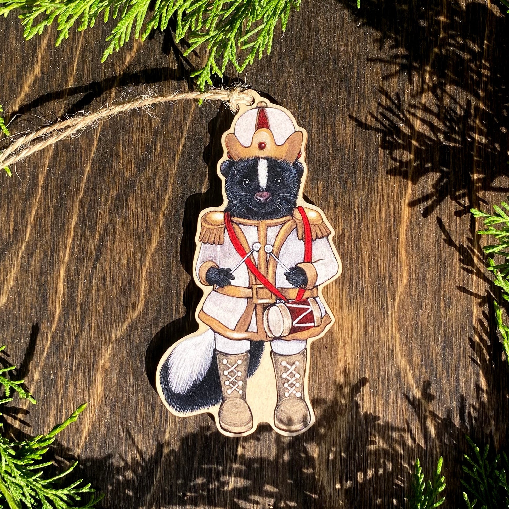 A wooden ornament strung with twine of a skunk in a white nutcracker outfit.