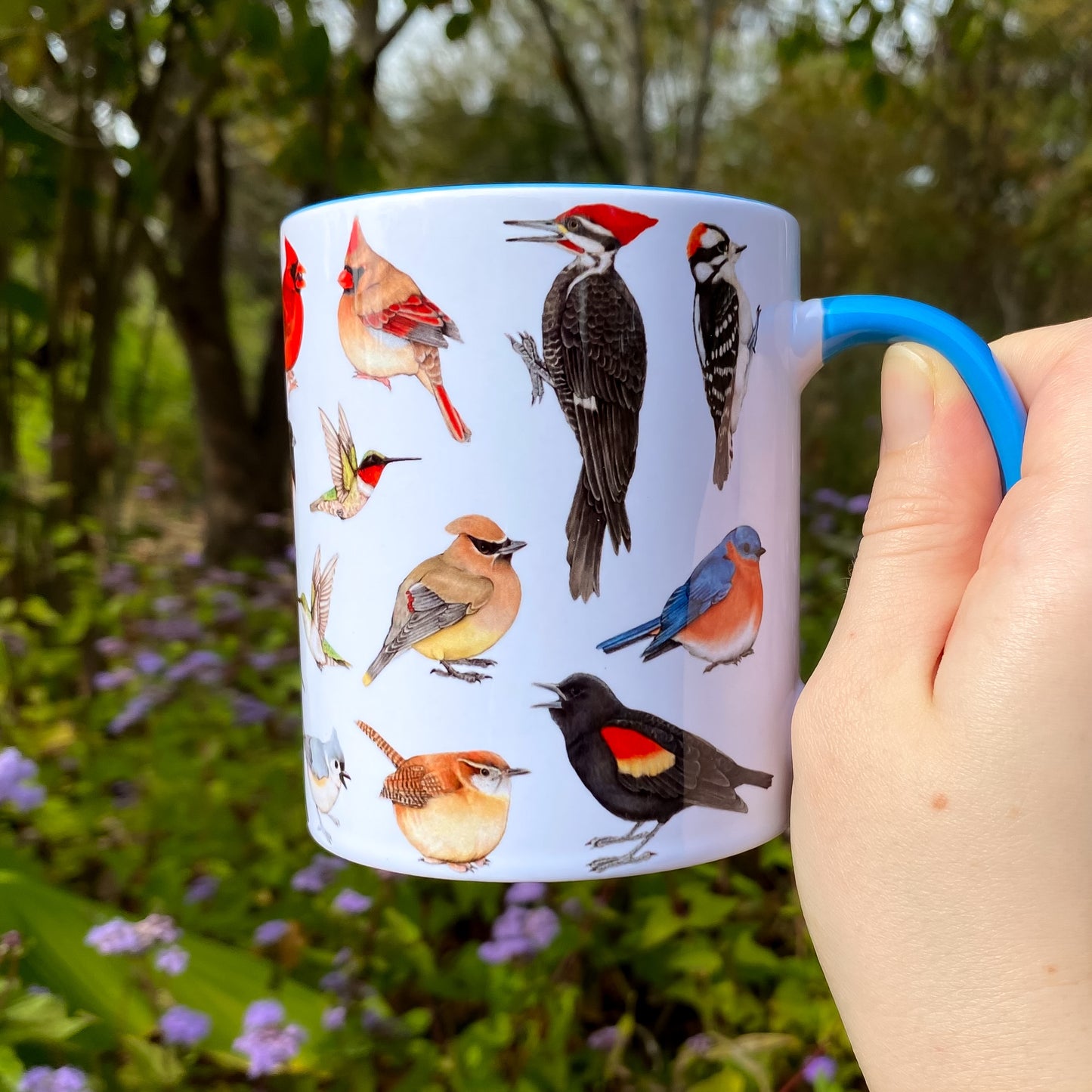 Mug with bird illustrations held in a hand against a natural background