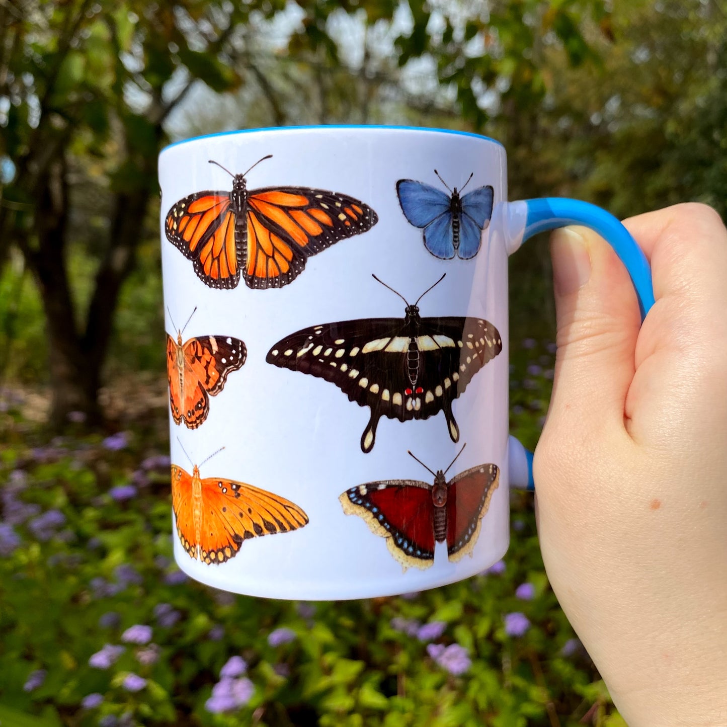 Mug with butterfly illustrations held by a hand in a garden setting