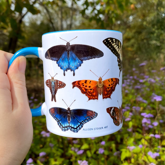 Mug with butterfly illustrations held by a hand in a natural setting