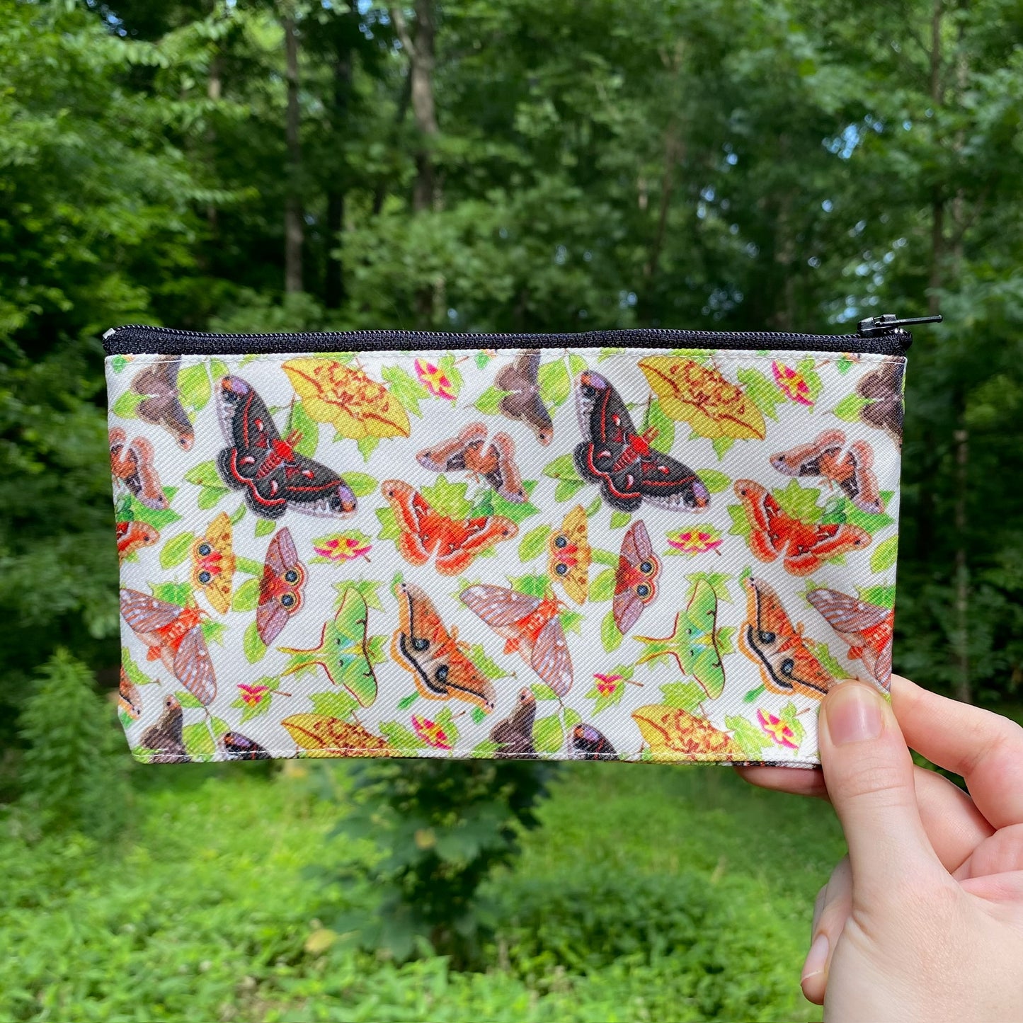 A hand holding a beige pouch with a pattern of silkmoths and leaves.