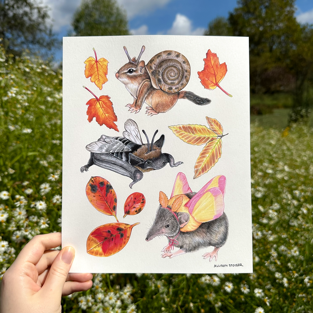 A hand holding a print featuring a spread a costumed chipmunk, bat, and shrew and fall foliage.