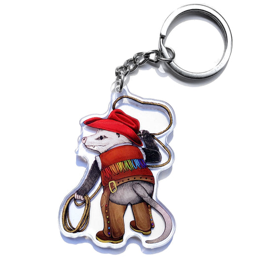 This double-sided acrylic keychain  features my illustration of an opossum cowhand showing off their lassoing skills and rainbow-fringed duds!