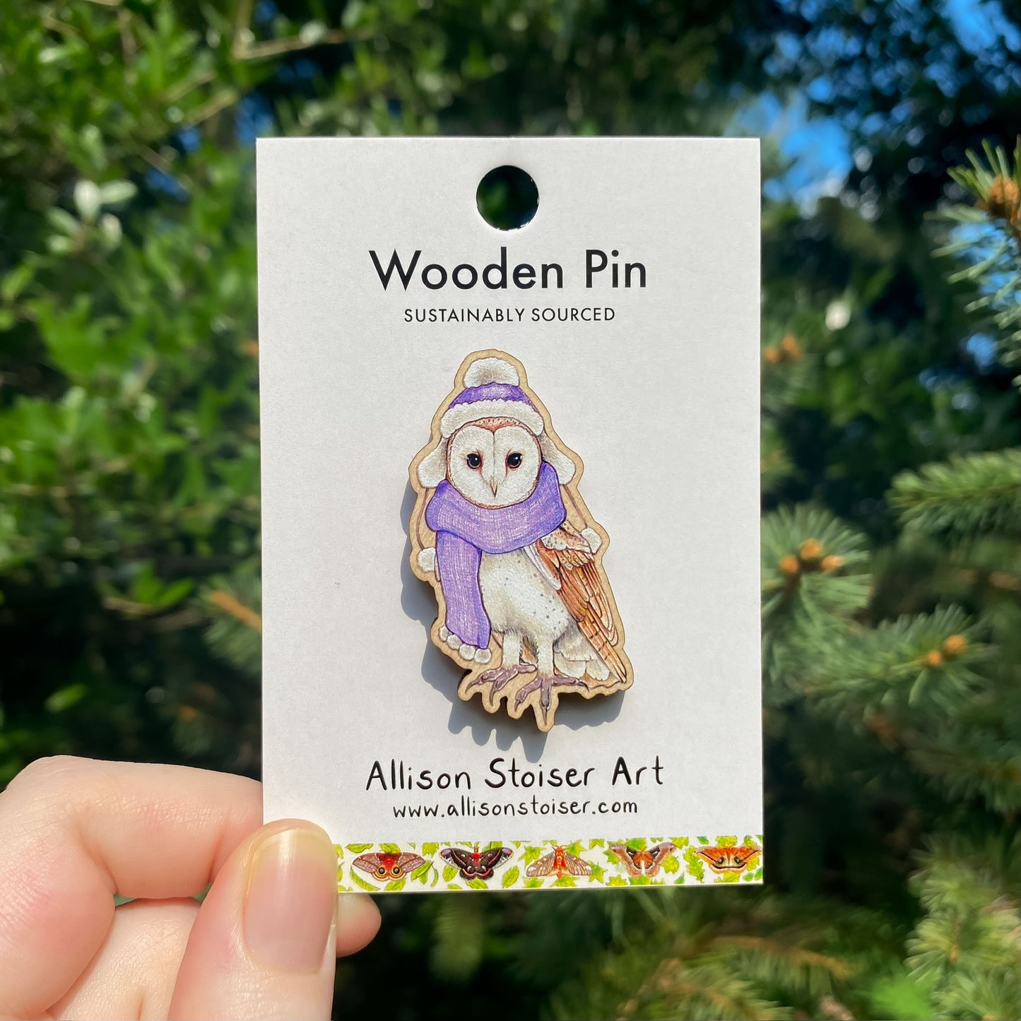 Wooden pin with a barn owl in a scarf on a card in front of green foliage