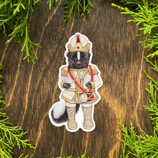 A weatherproof vinyl sticker of a skunk dressed in a white nutcracker outfit surrounded by cedar foliage.