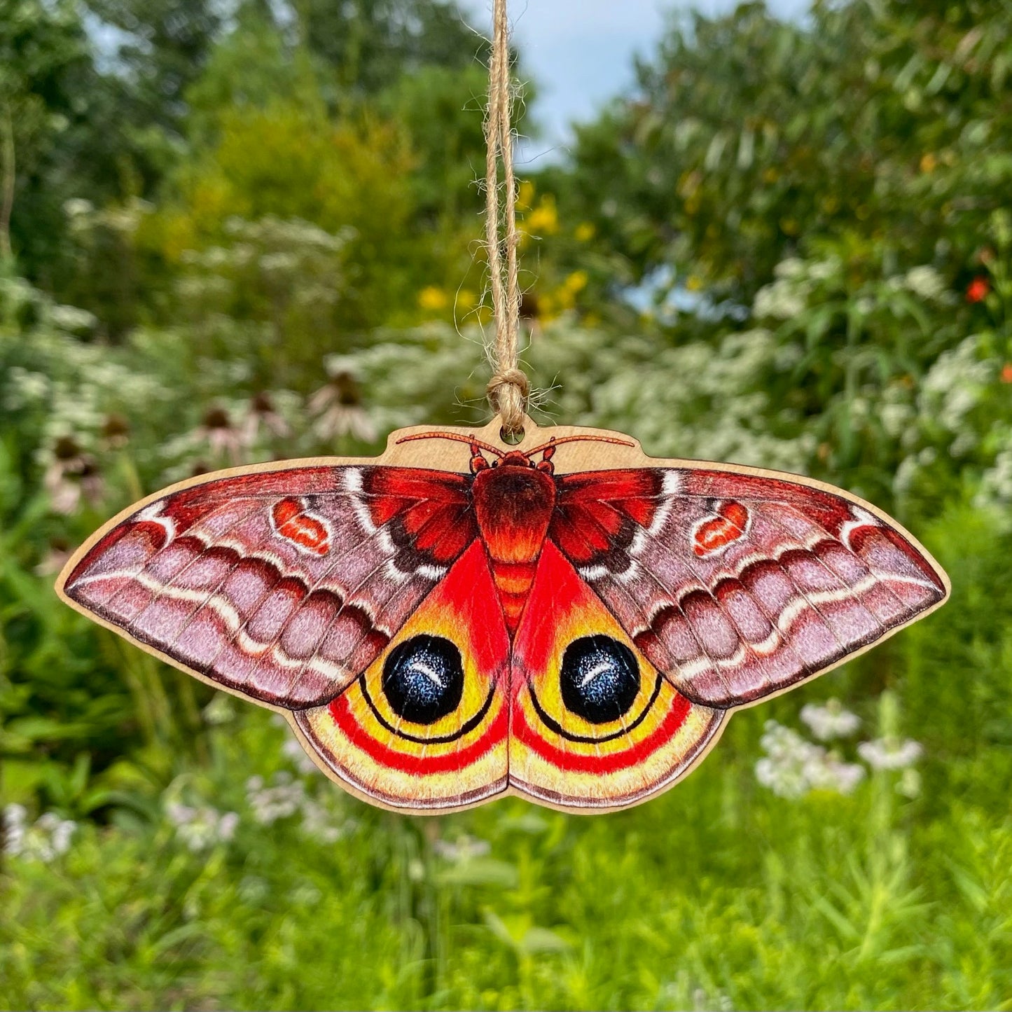 A wooden ornament strung with twine of a female io moth.