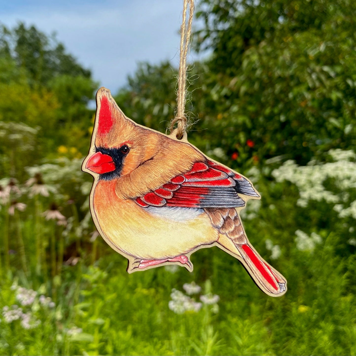 A wooden ornament strung with twine of a female North American cardinal.