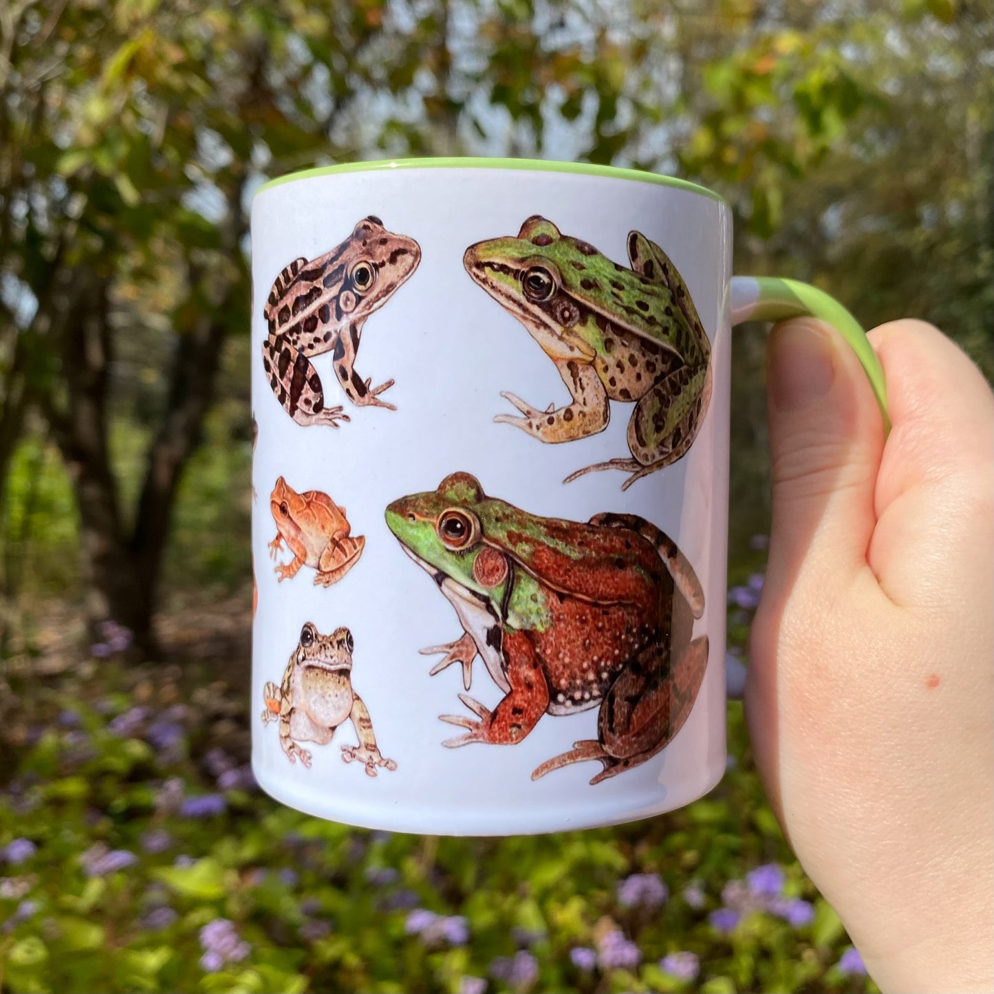 Mug with frog illustrations held in a hand outdoors