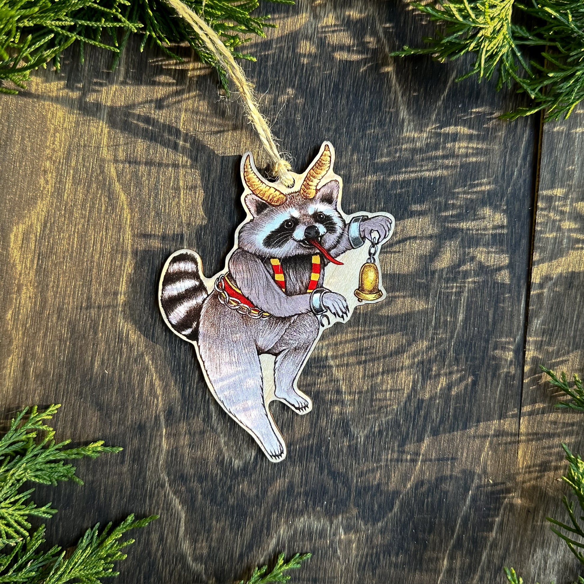 An ornament of a raccoon dressed up as Krampus holding a bell.