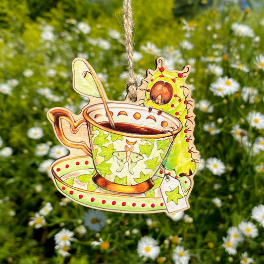 ornament of a teacup with a luna moth caterpillar sitting at the rim in front of a background of white flowers
