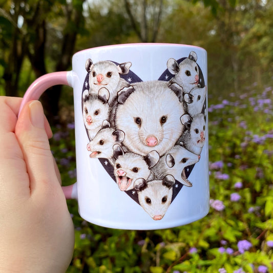Mug with opossum illustrations held by a hand in a natural setting