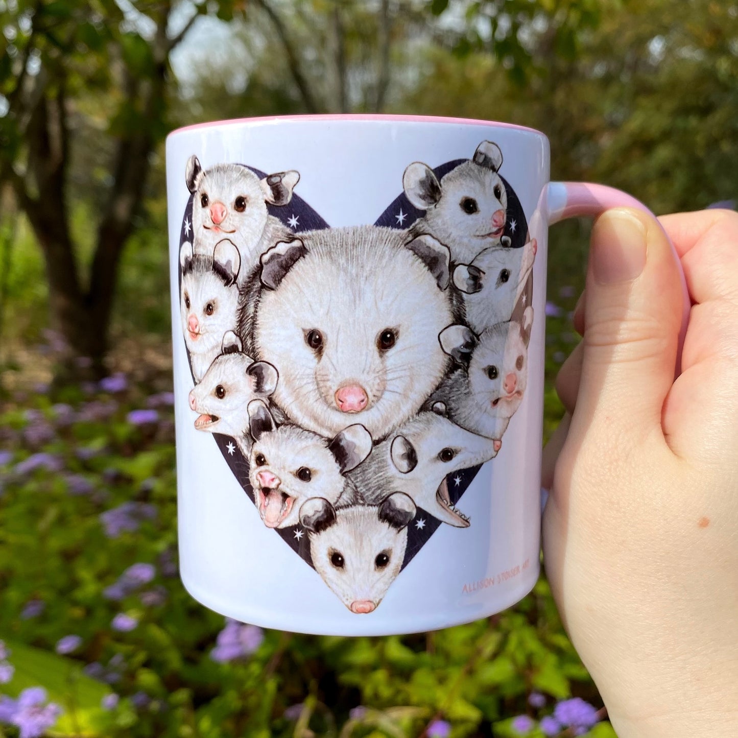Mug with opossum illustrations held in front of a natural background