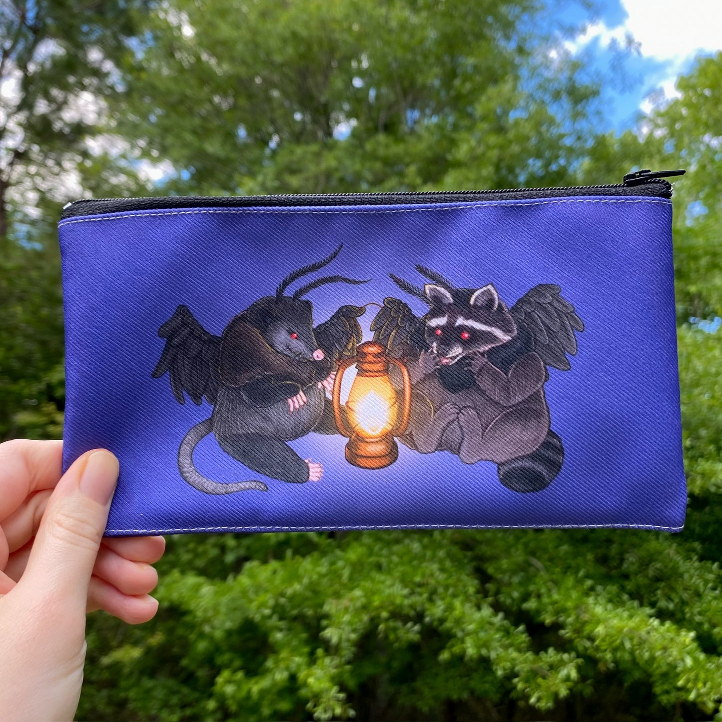 A dark purple zippered pouch with a drawing of a raccoon and an opossum dressed as mothman