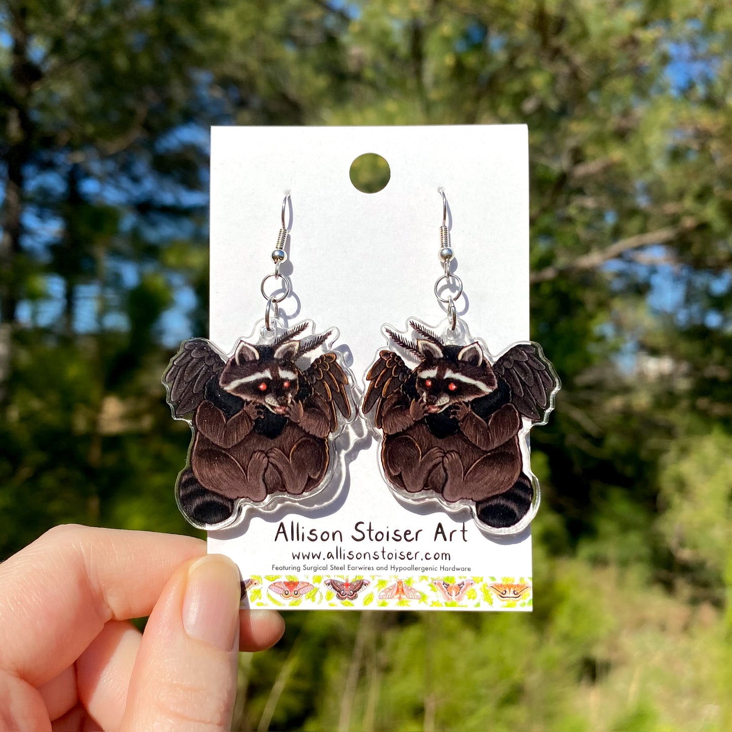 Earrings with acrylic charms of raccoons dressed up as mothman