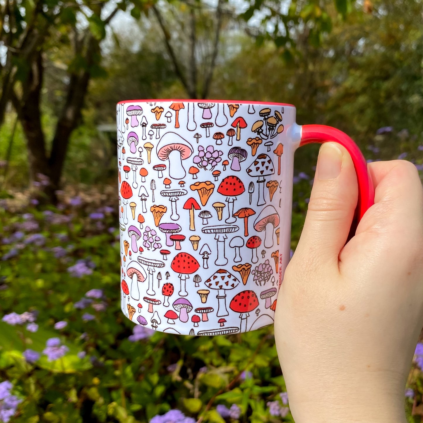 Mug with mushroom pattern held by a hand against a natural background
