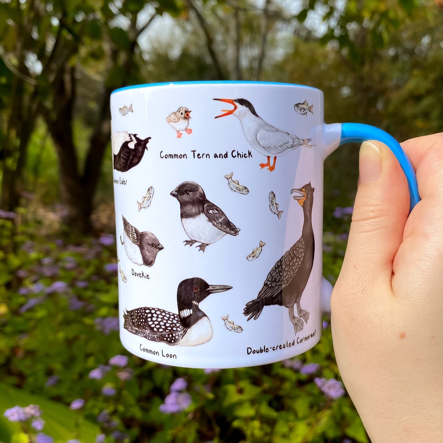 Mug with north Atlantic seabird illustrations held in a hand outdoors