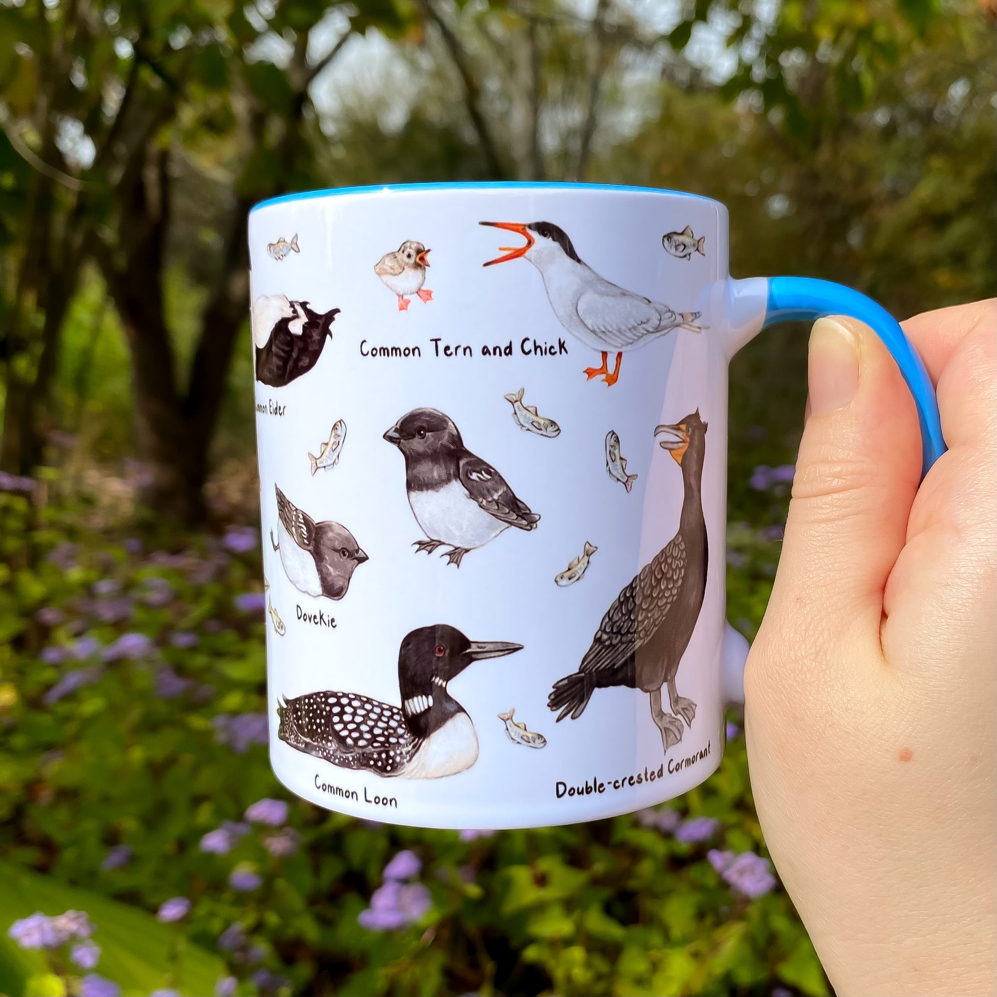 Mug with north Atlantic seabird illustrations held in a hand outdoors