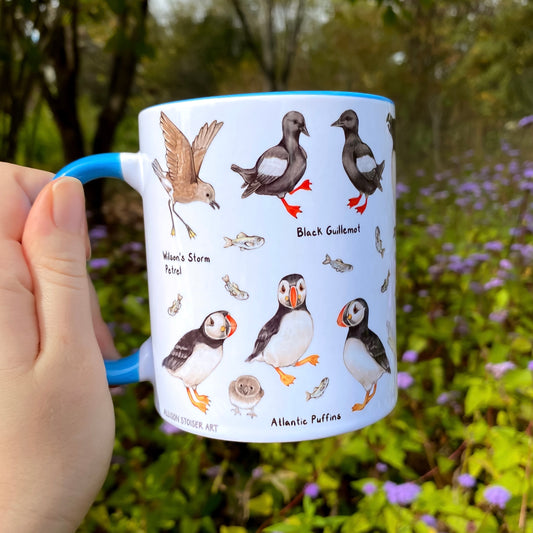Mug with North Atlantic seabird illustrations held by a hand in a garden setting