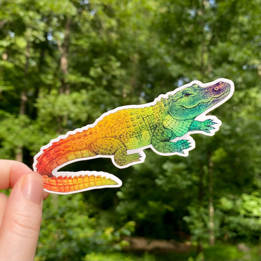A hand holding a rainbow holo sticker of an American alligator.