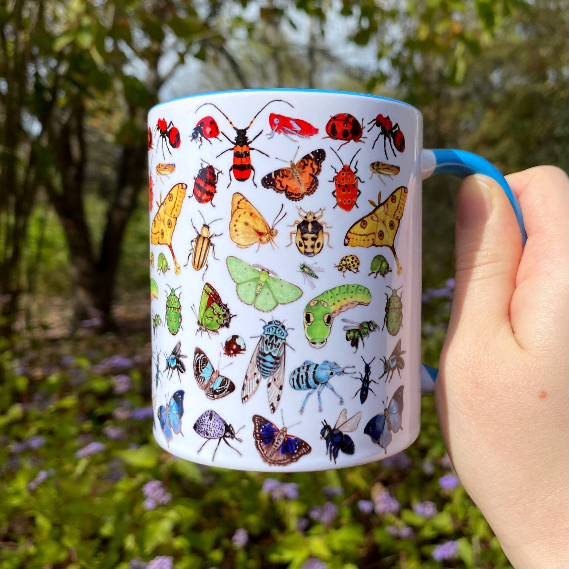 Mug with insect illustrations held in a hand outdoors