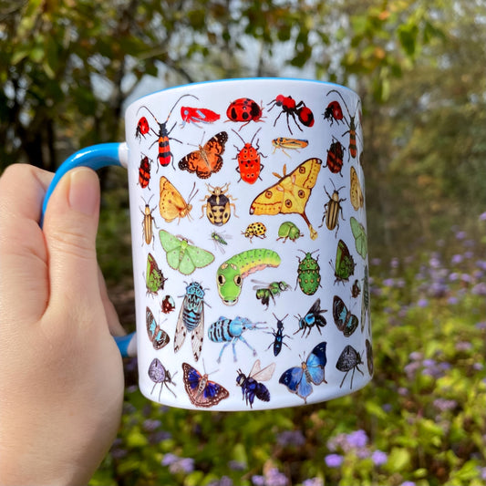 Mug with insect illustrations held by a hand against a natural background