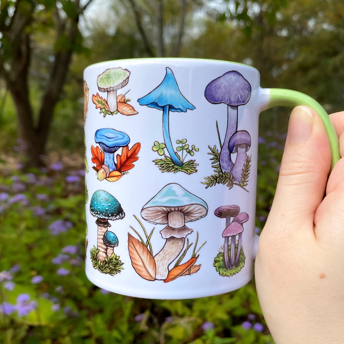 Mug with mushroom illustrations held in a hand against a natural background