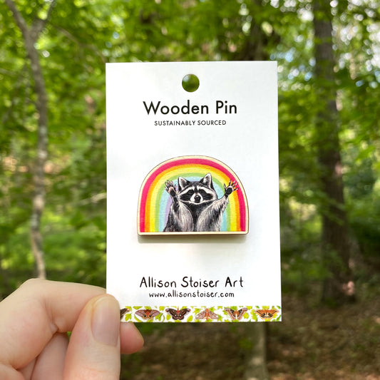 A wooden pin of a raccoon in front of a rainbow