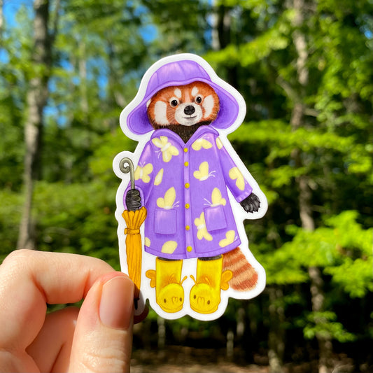 A sticker of a red panda in a purple raincoat with butterflies and yellow rain boots. She's holding a yellow umbrella at her side.