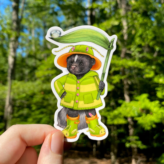 a sticker of a skunk with rainboots and in a green and yellow striped raincoat. He's holding a blade of grass.