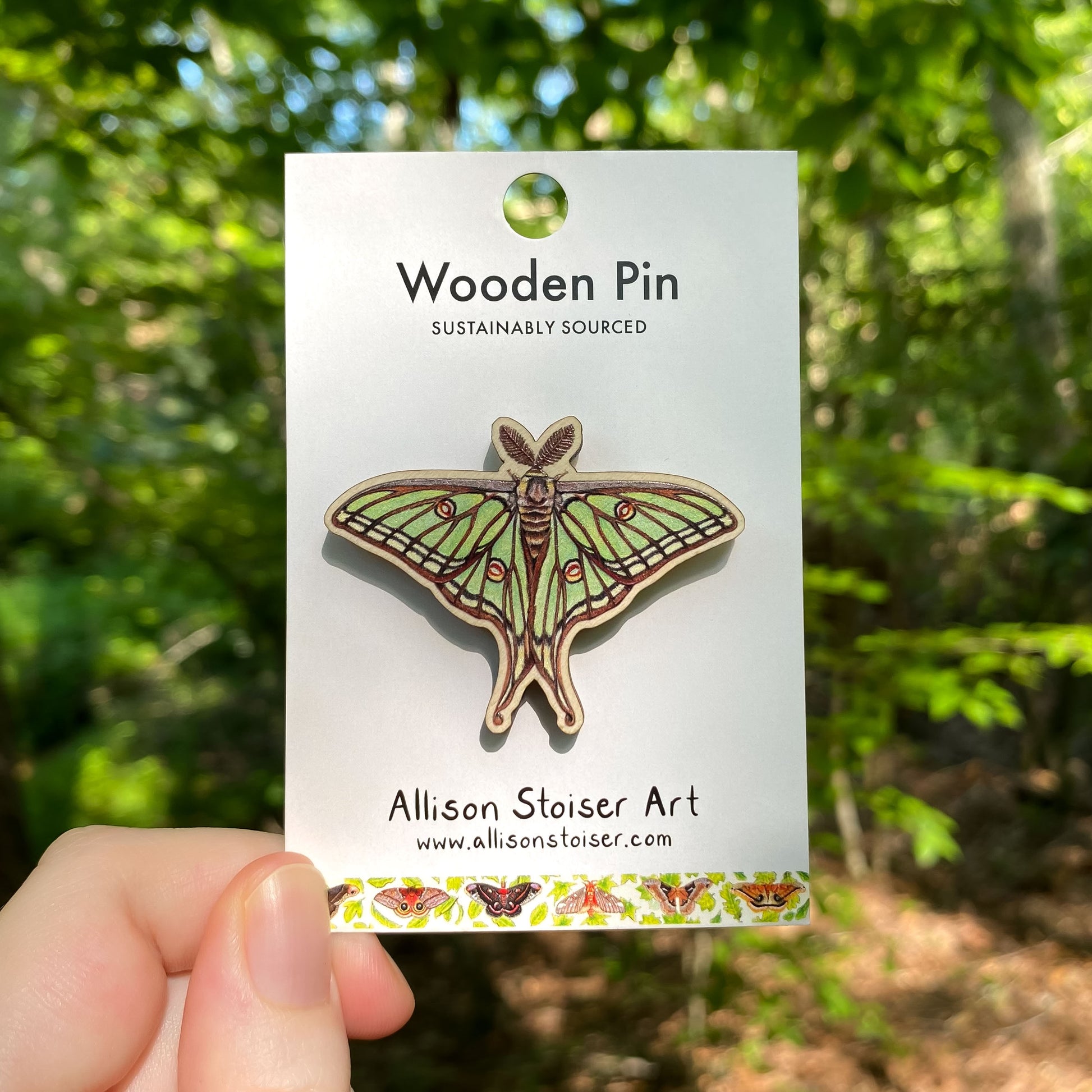 A wooden pin of a Spanish moon moth on packaging that reads Wooden Pin, Sustainably Sourced.