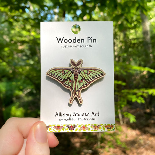 A wooden pin of a Spanish moon moth on packaging that reads Wooden Pin, Sustainably Sourced.