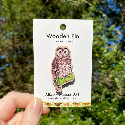 Wooden pin of a spotted owl on a card held by a hand with a natural background