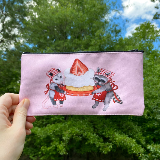 A pink separate pouch with an illustration of a raccoon and an opossum holding a strawberry cake