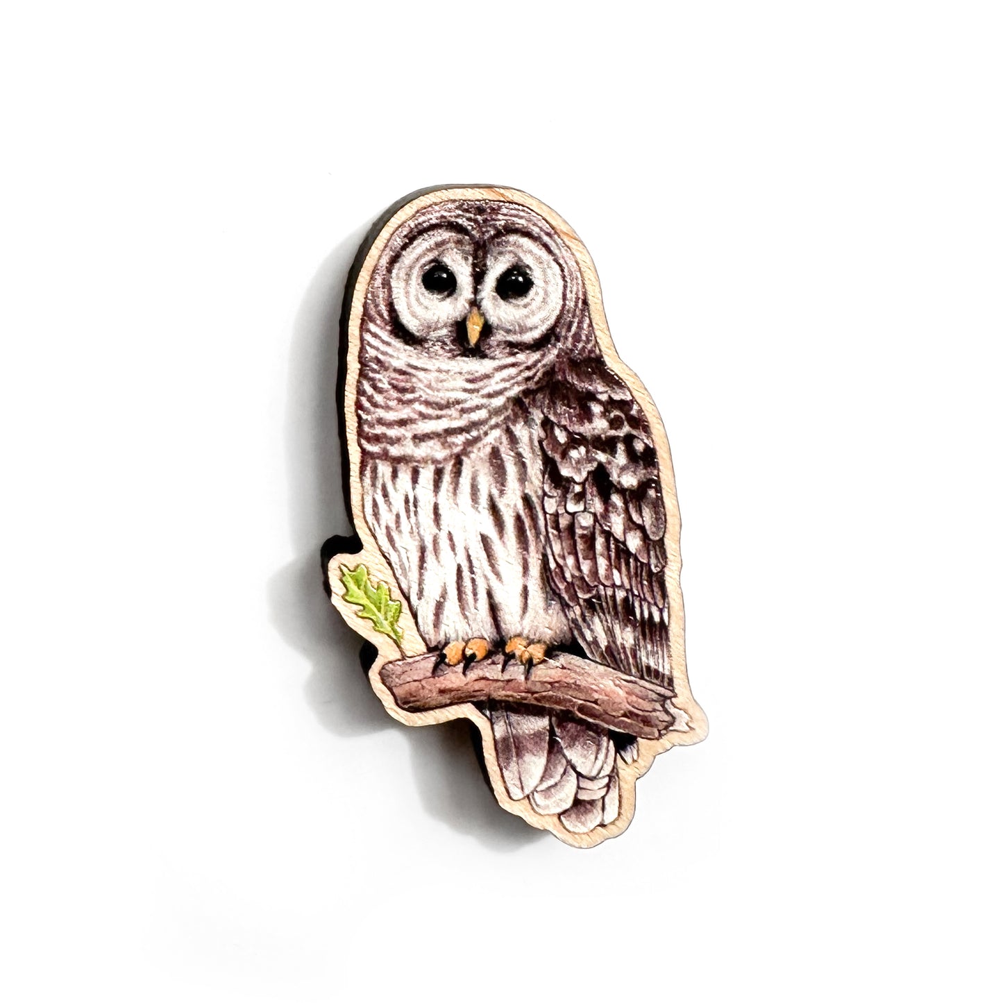 A wooden pin of a barred owl on a white background.