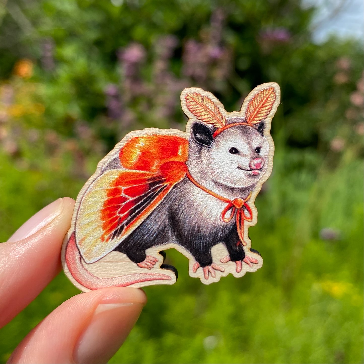 A sustainably sourced wooden pin featuring an opossum dressed as a flannel moth