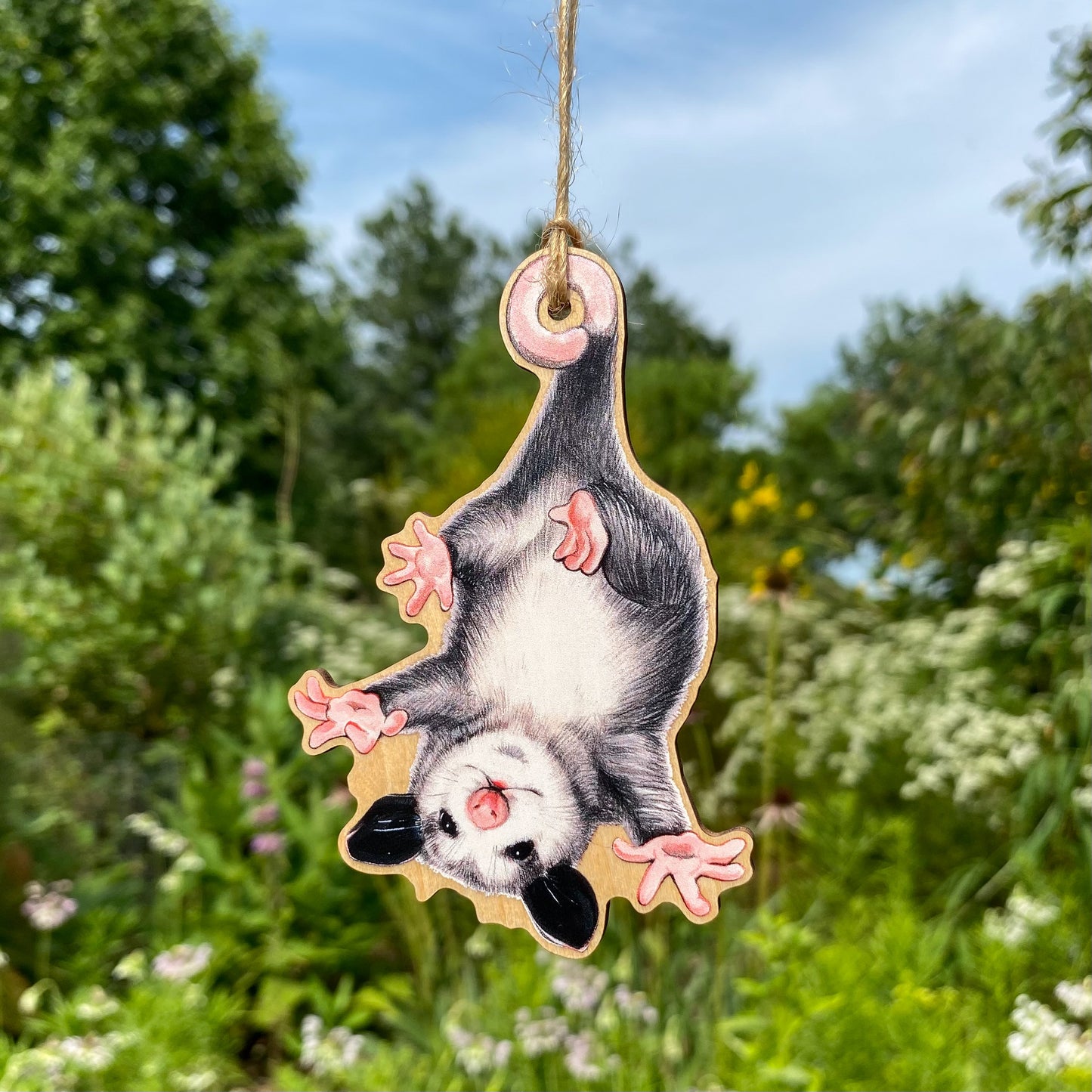 A wood print ornament featuring an illustration of a baby opossum