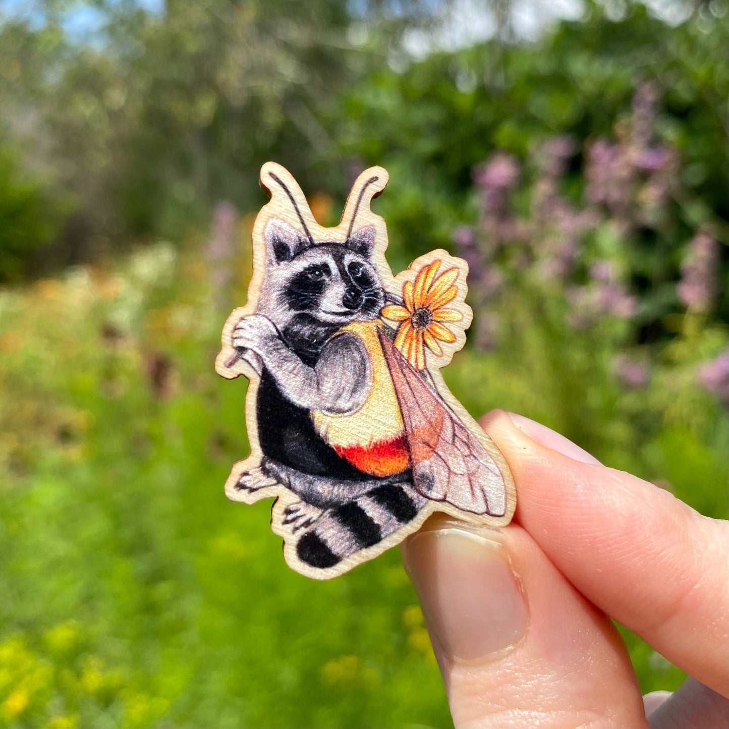 A sustainably sourced wooden pin featuring a raccoon dressed as a bee