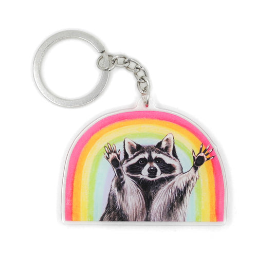 A keychain featuring a raccoon with raised hands posed in front of a rainbow