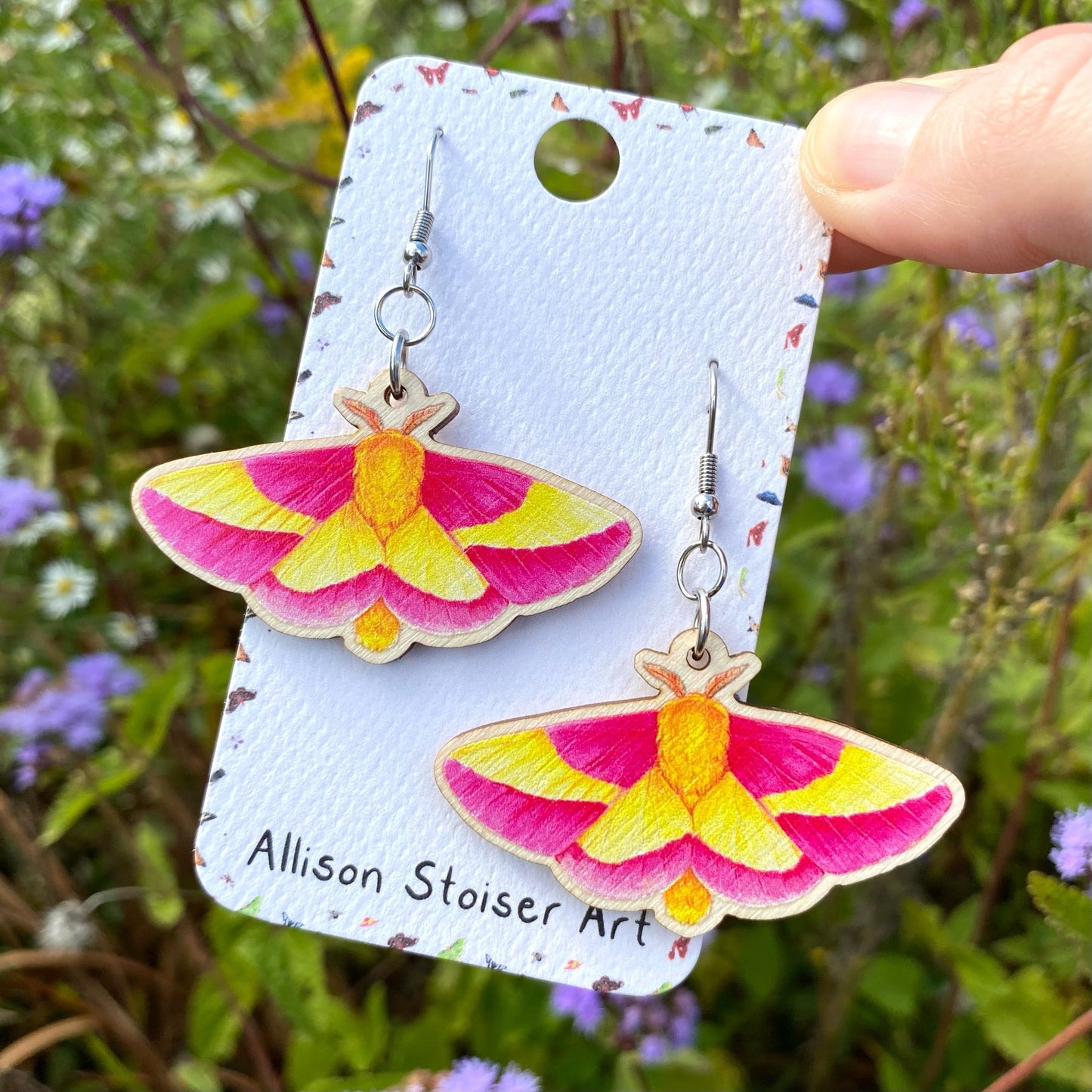 A hand holding a pair of rosy maple moth earrings