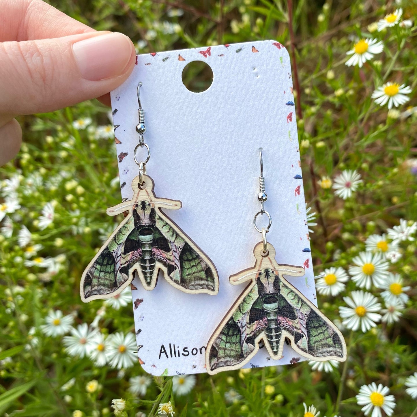 A hand holding a pair of pandorus sphinx moth earrings