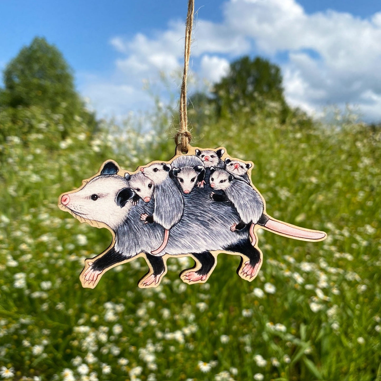 A wooden ornament strung with twine of a mom opossum running to the side with babies on her back.