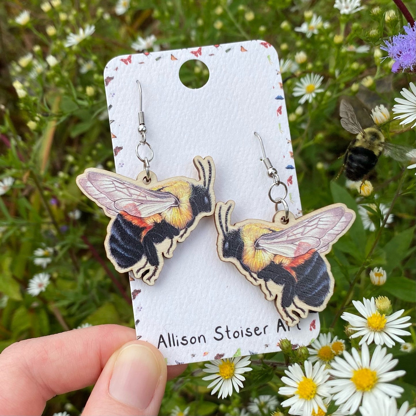 A hand holding a pair of brown-belted bumblebee earrings