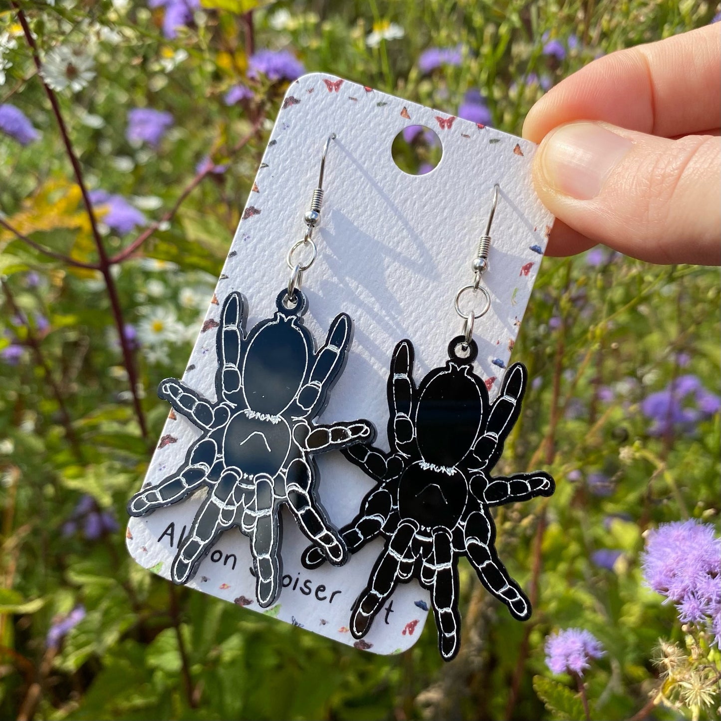 A hand holding a pair of black acrylic tarantula earrings