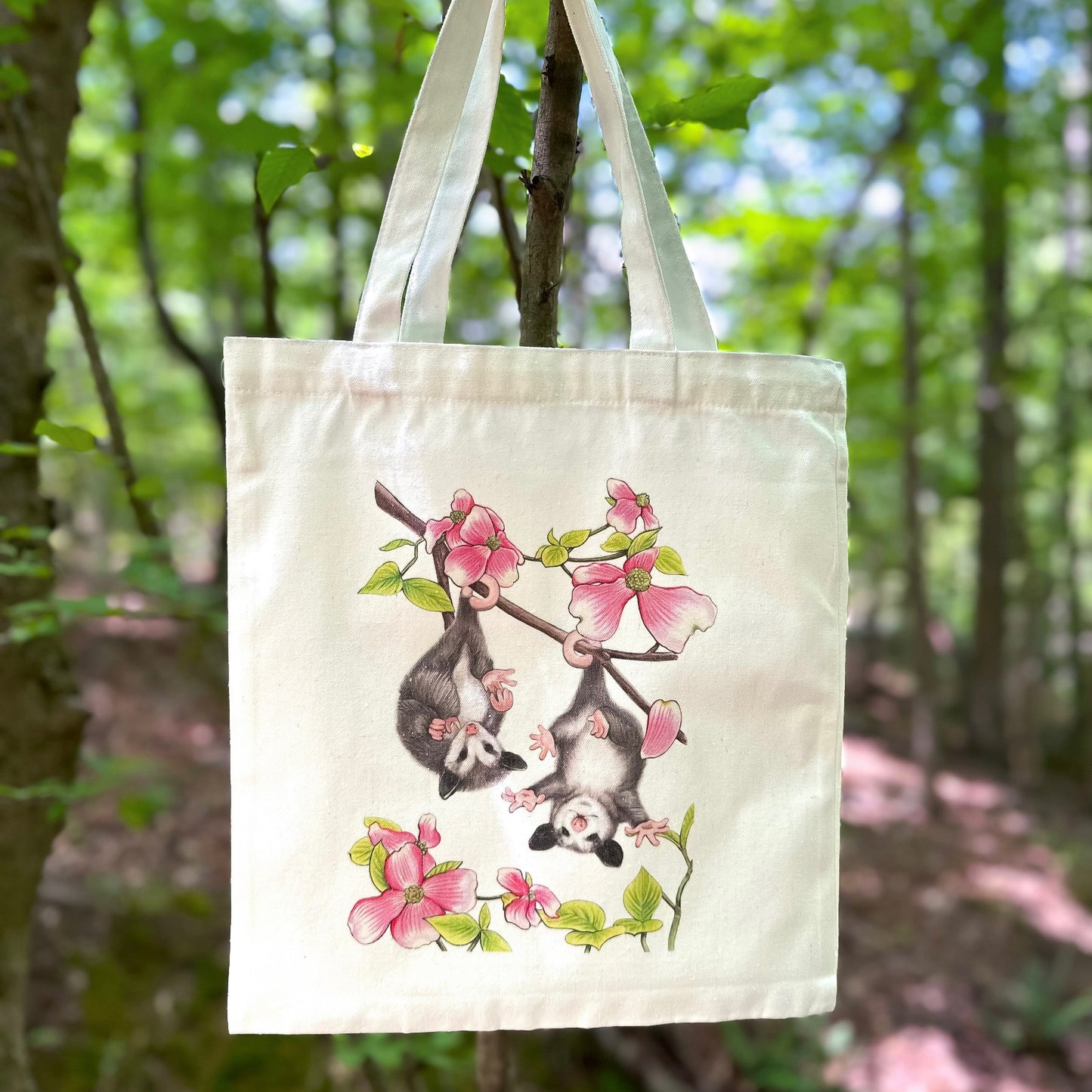 A totebag featuring an illustration of baby opossums in dogwood